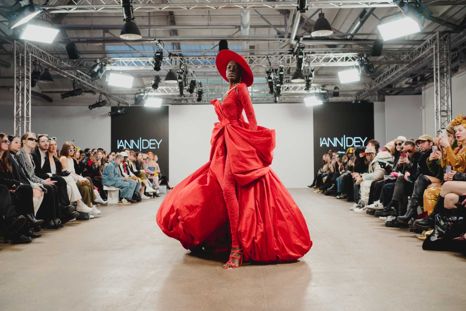 Modelo en pasarela con vestido rojo dramático, evento de moda