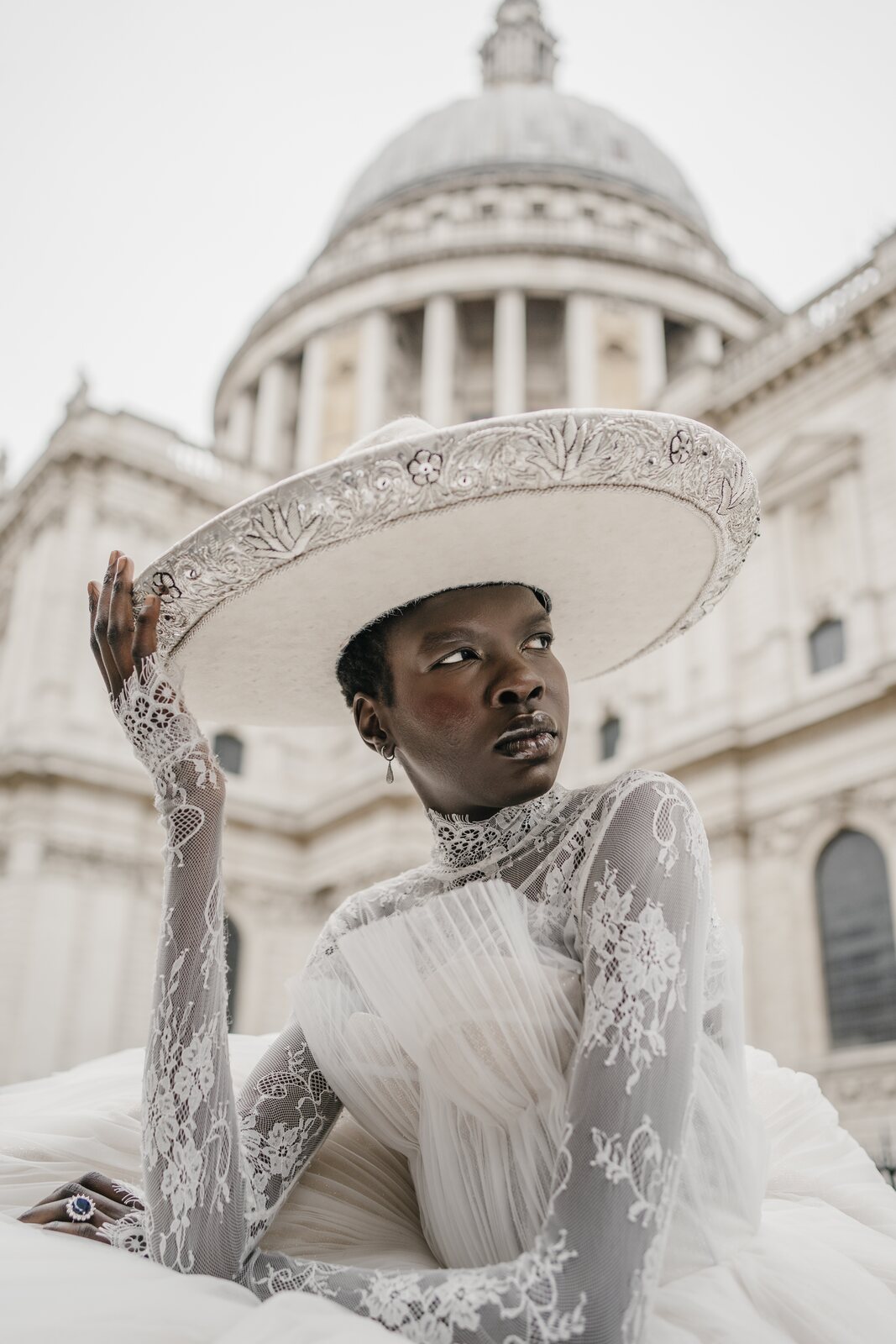 Retrato editorial de una mujer con sombrero y vestido de encaje blanco frente a un edificio con cúpula