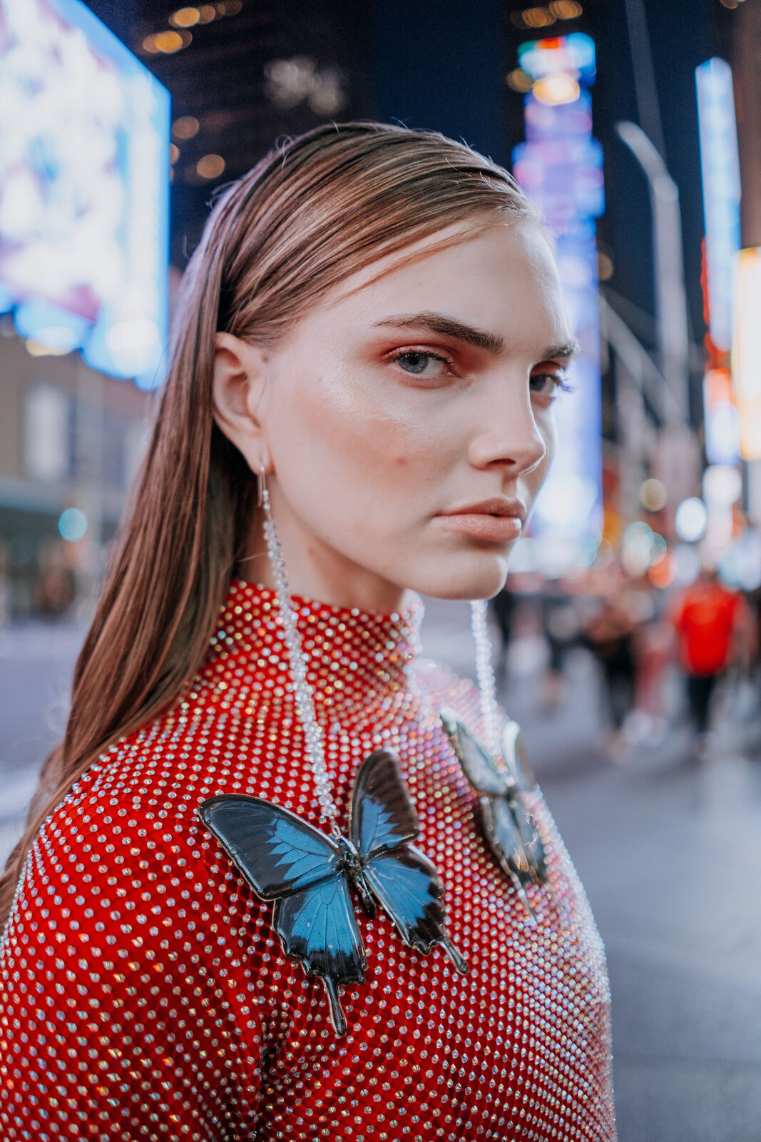 Retrato de una mujer con vestido rojo y aretes de mariposa en una calle iluminada de noche